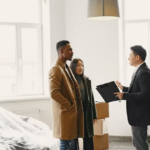 Three individuals conversing indoors in a newly furnished house with furniture still covered