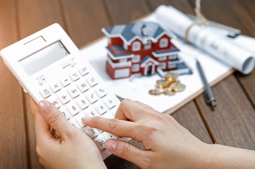 hands holding and pressing on calculator, toy house behind on the table