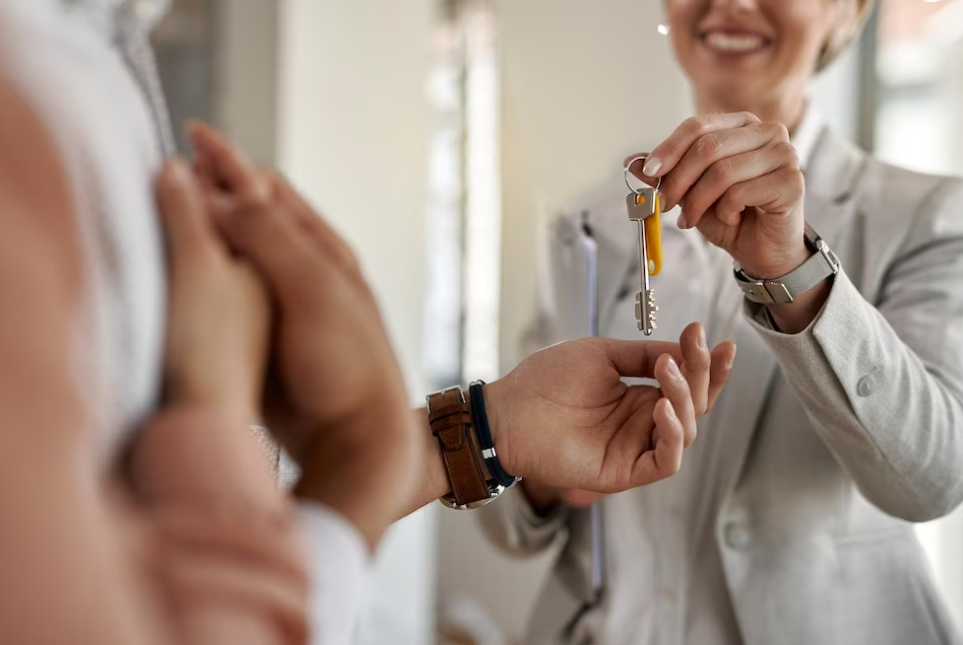 smiling woman in a gray suit passes the keys to a man with a watch