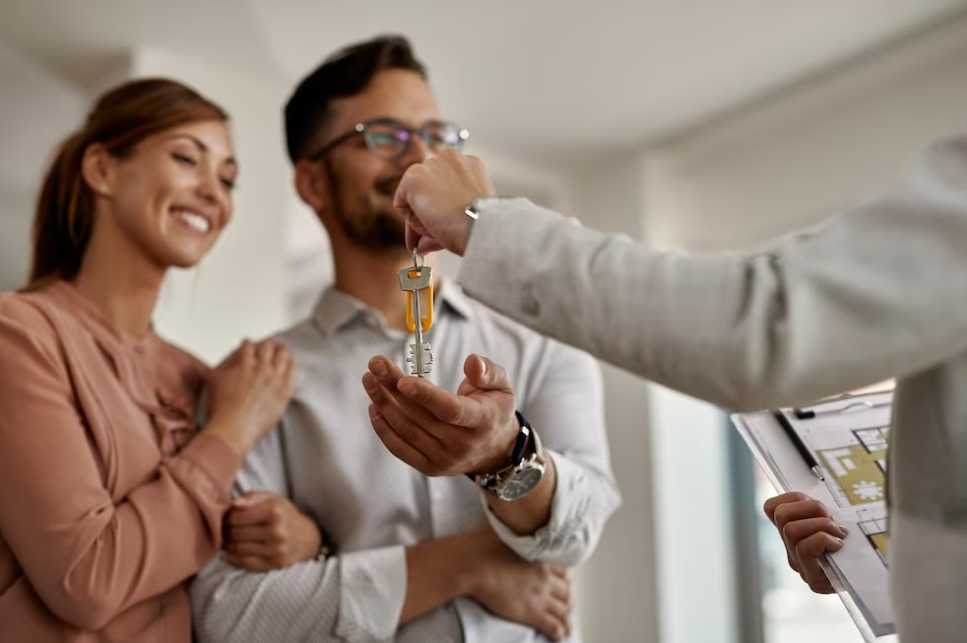 person passing keys to a smiling couple of woman and man