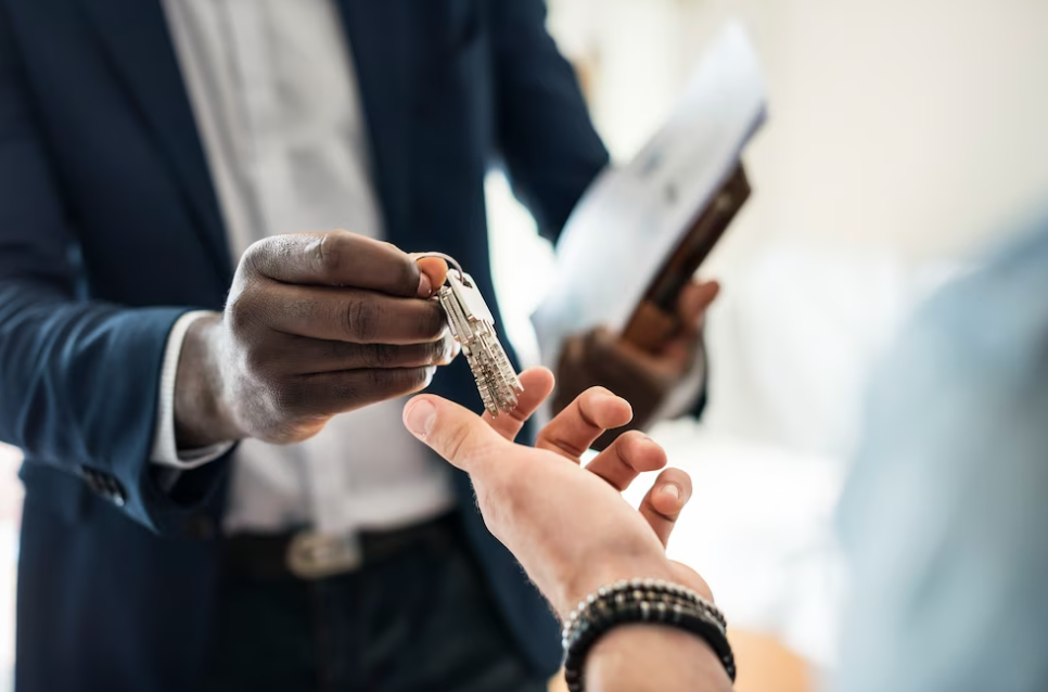 man in dark blue suit passes the keys to man with bracelet