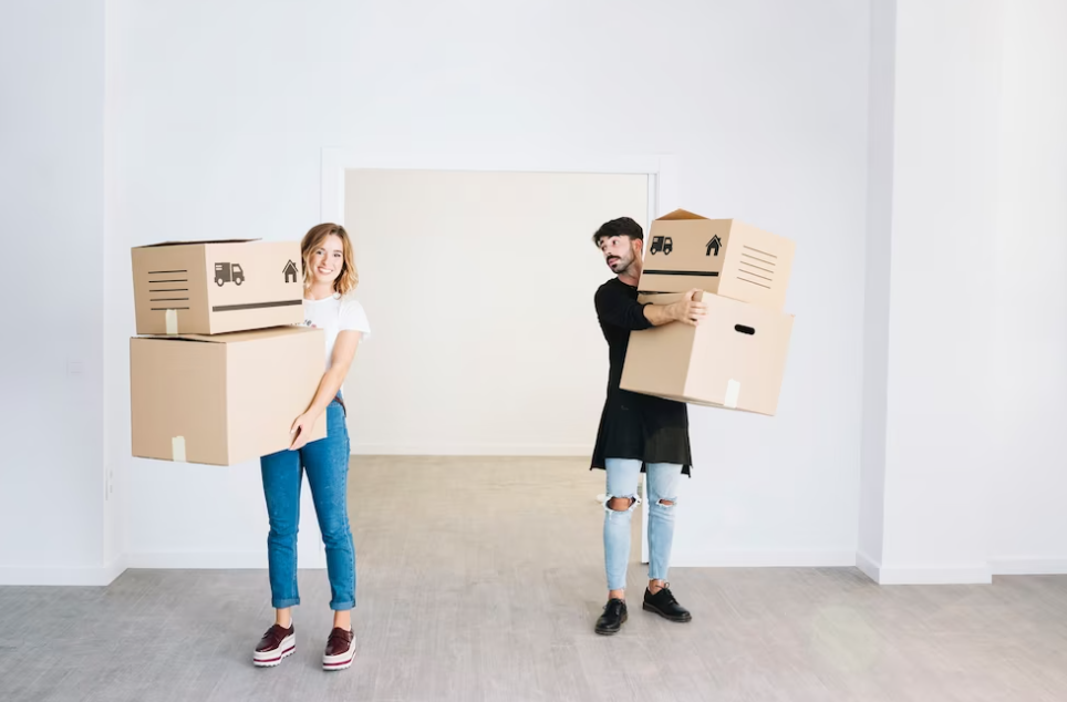 man and woman holding boxes in empty room, man looks at her